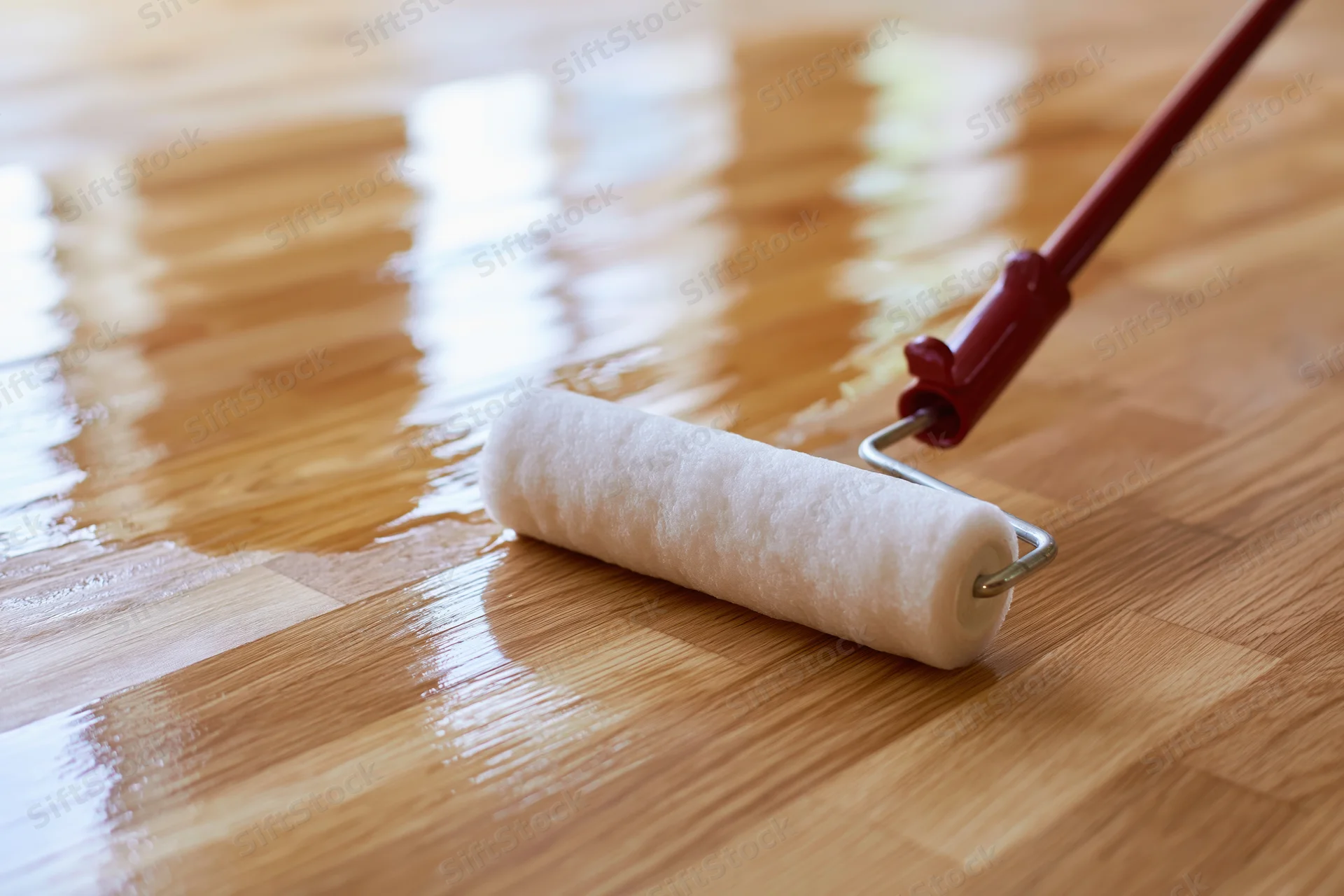 Paint roller applying clear varnish to hardwood floor