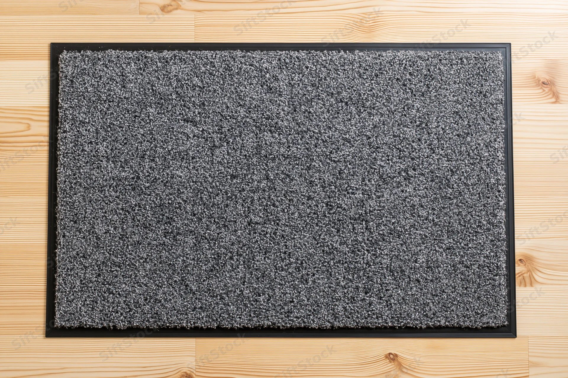 Grey doormat with black rubber border lying flat on light wooden flooring