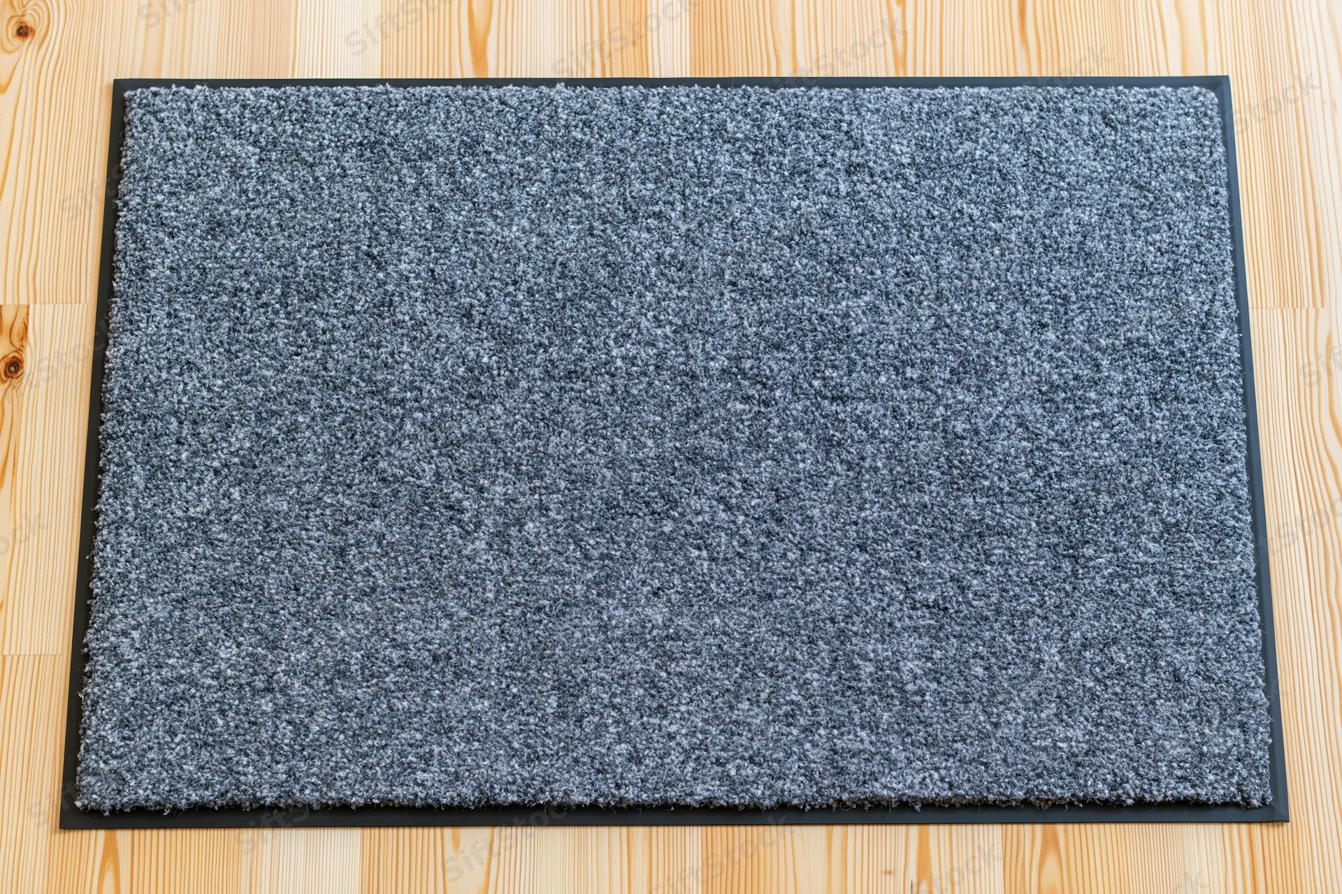 Rectangular grey doormat with black rubber border lying on light wood flooring