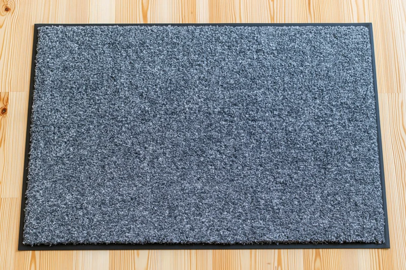 Rectangular grey doormat with black rubber border lying on light wood flooring