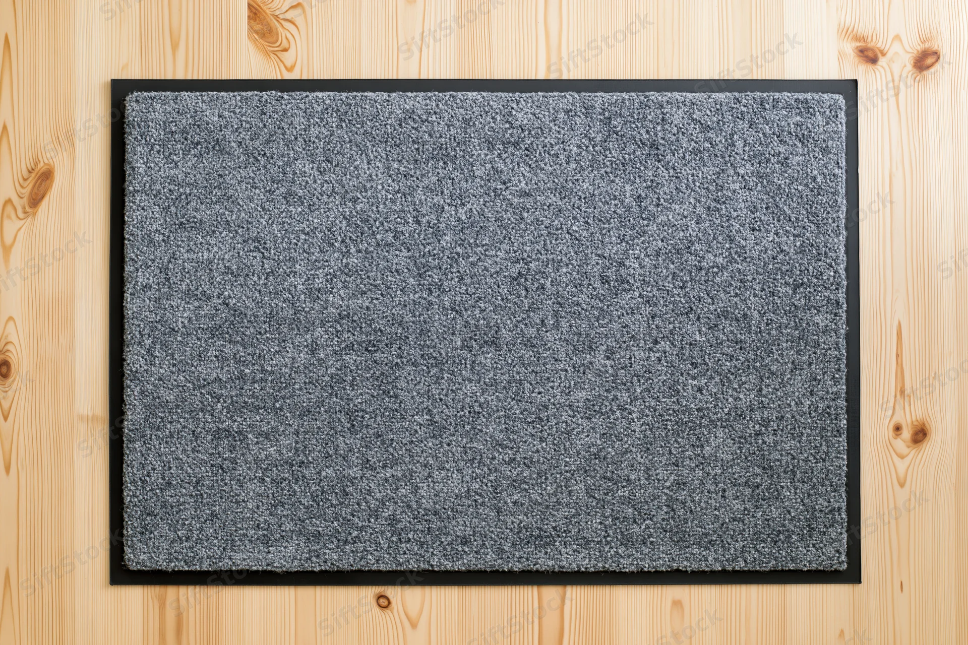 Grey doormat with black rubber border lying flat on wooden floor