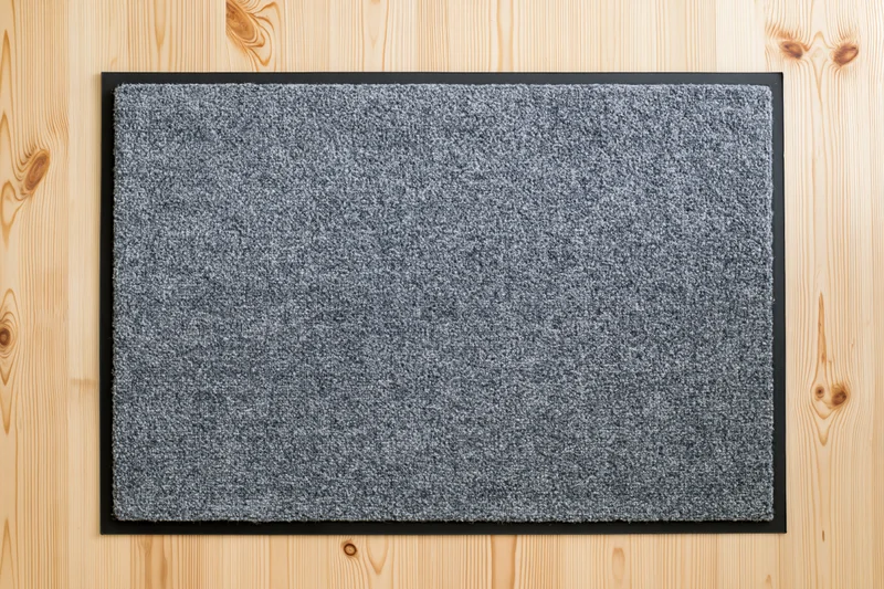 Grey doormat with black rubber border lying flat on wooden floor