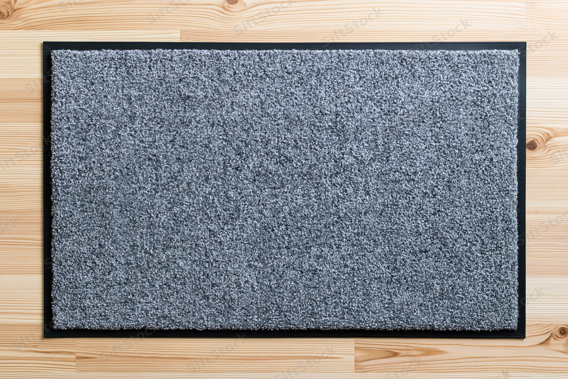 Grey rectangular doormat with black rubber border lying on light wood flooring