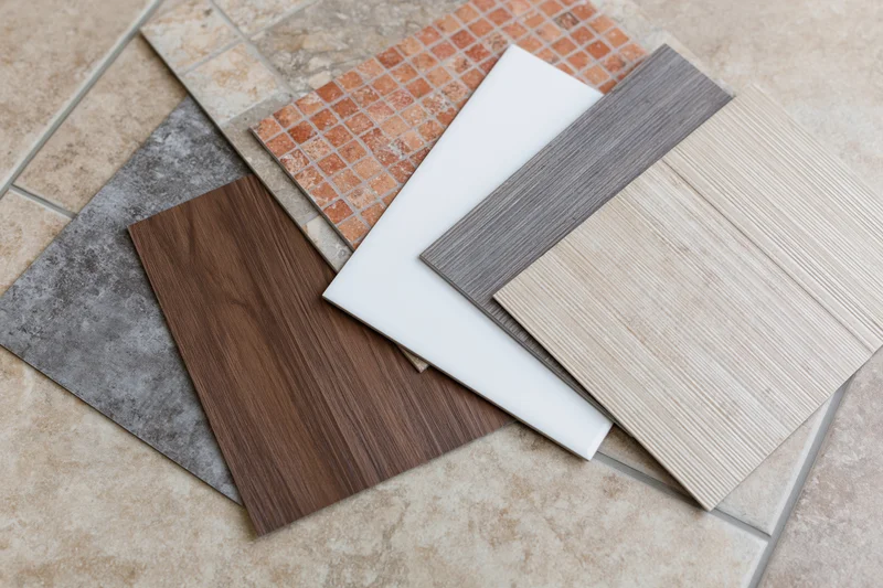 Flooring and tile sample squares fanned out on a tiled surface for selection and design planning