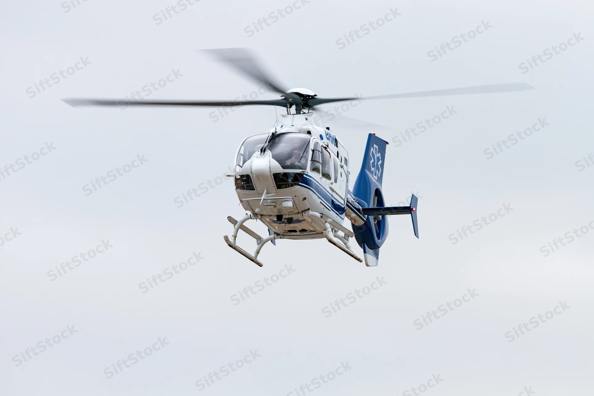 White and blue medical helicopter hovering in overcast sky