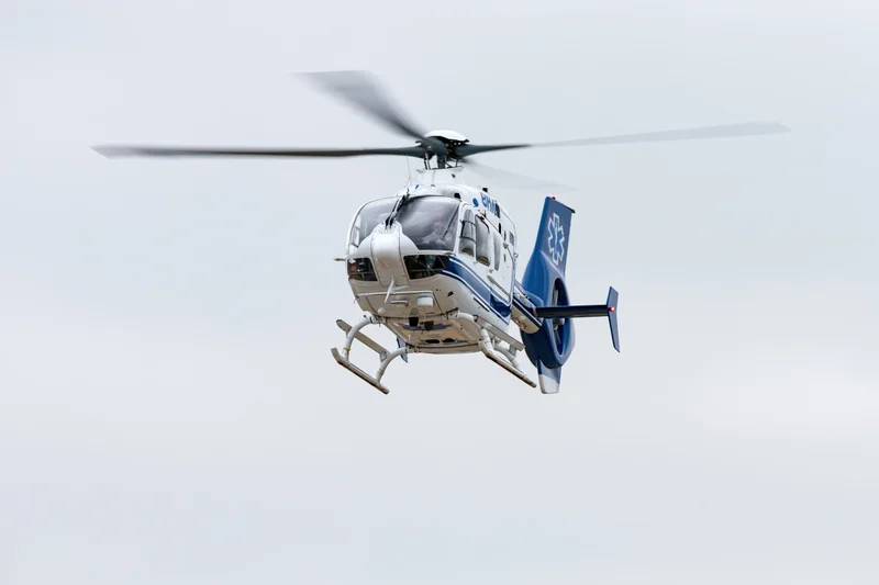 White and blue medical helicopter hovering in overcast sky