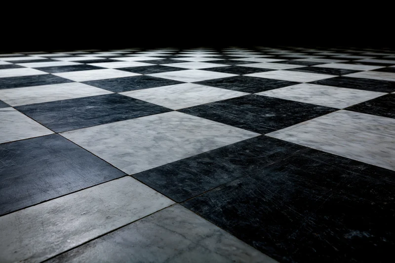 Aged black and white marble checkerboard floor extending into perspective with visible wear and grout lines