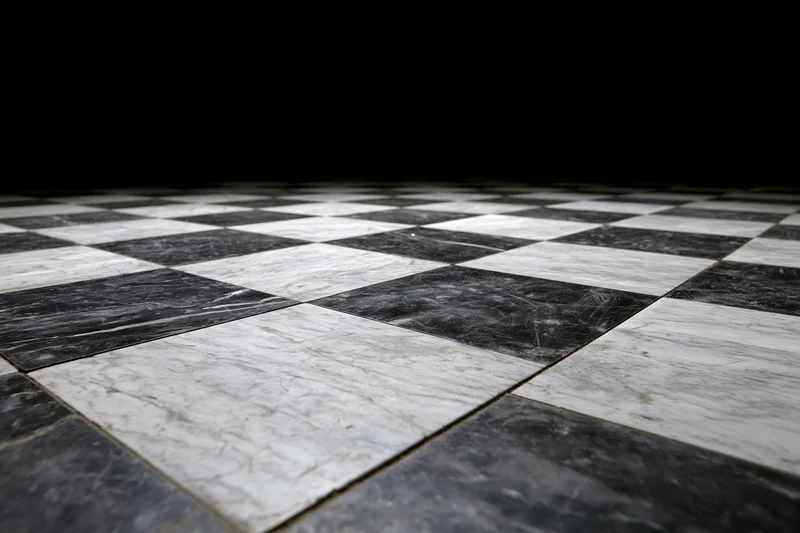 Aged black and white marble checkerboard floor extending into the distance with dark background and copyspace