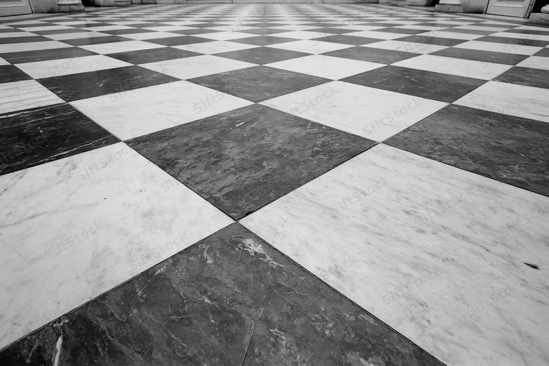 Aged black and white marble checkerboard floor tiles arranged in a receding geometric pattern inside a spacious interior