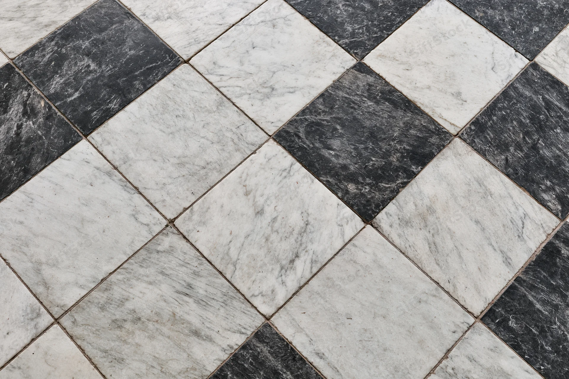 Aged black and white marble tiles arranged diagonally on a floor