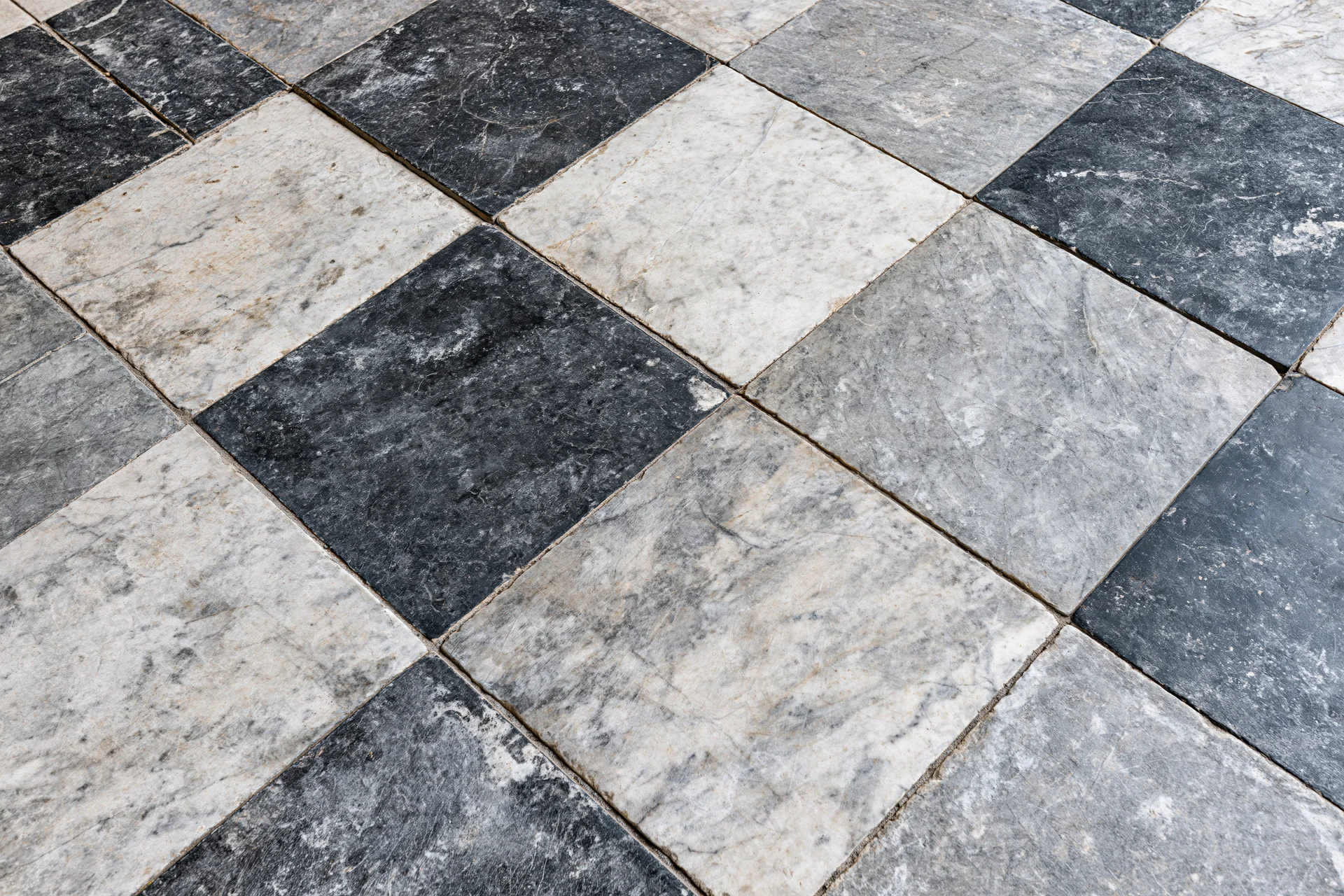 Aged black and white marble tiles arranged diagonally on a floor