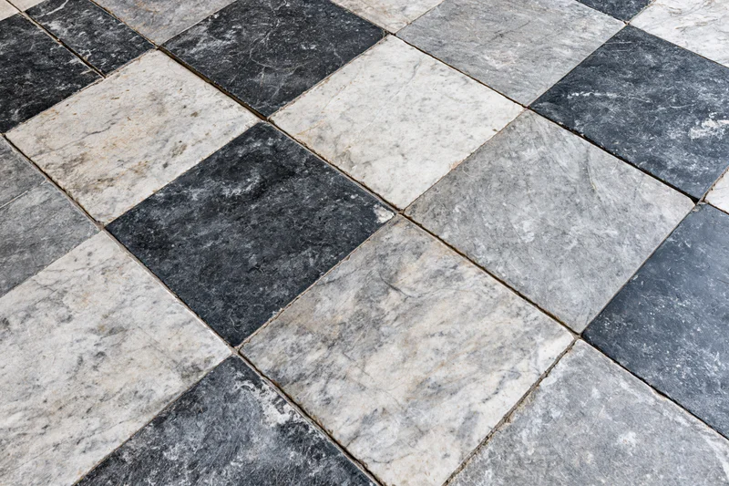 Aged black and white marble tiles arranged diagonally on a floor