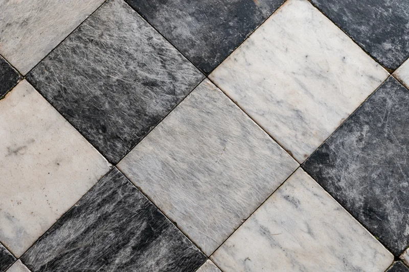 Aged black and white marble floor tiles arranged diagonally in a checkered pattern