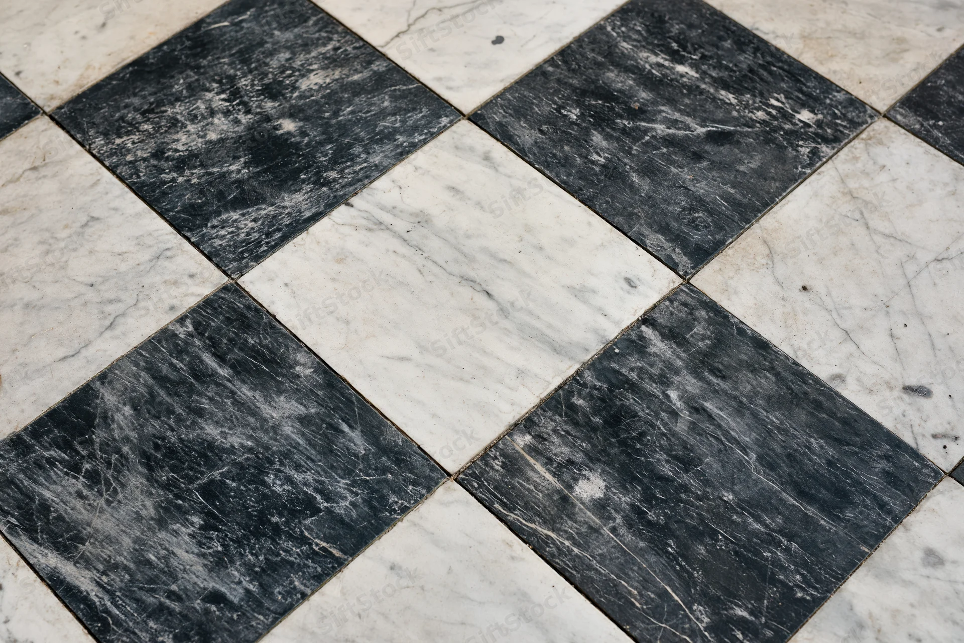Aged black and white marble floor tiles arranged diagonally in a checkered pattern