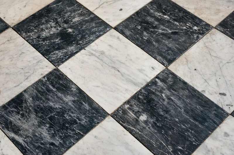 Aged black and white marble floor tiles arranged diagonally in a checkered pattern