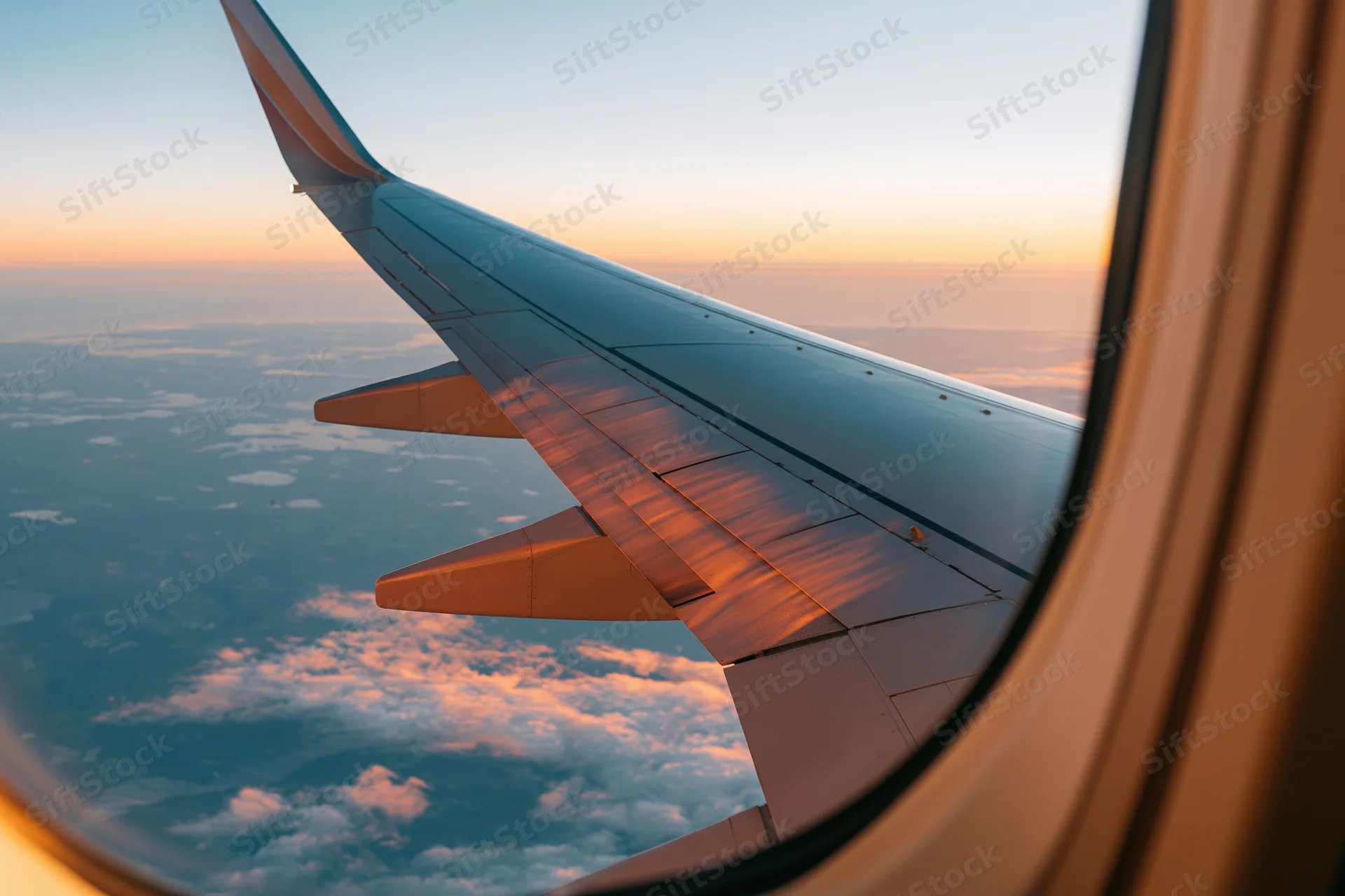 Airplane wing visible through passenger window during sunset flight at high altitude