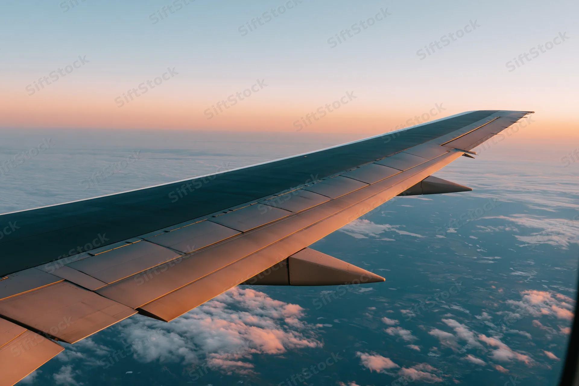 Airplane wing viewed through passenger window during high-altitude flight at sunset