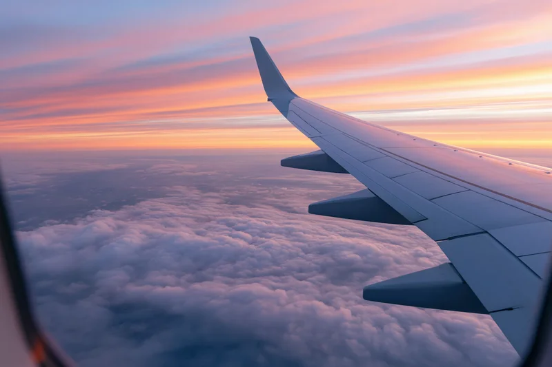 Airplane wing viewed through passenger window above cloud layer during sunset