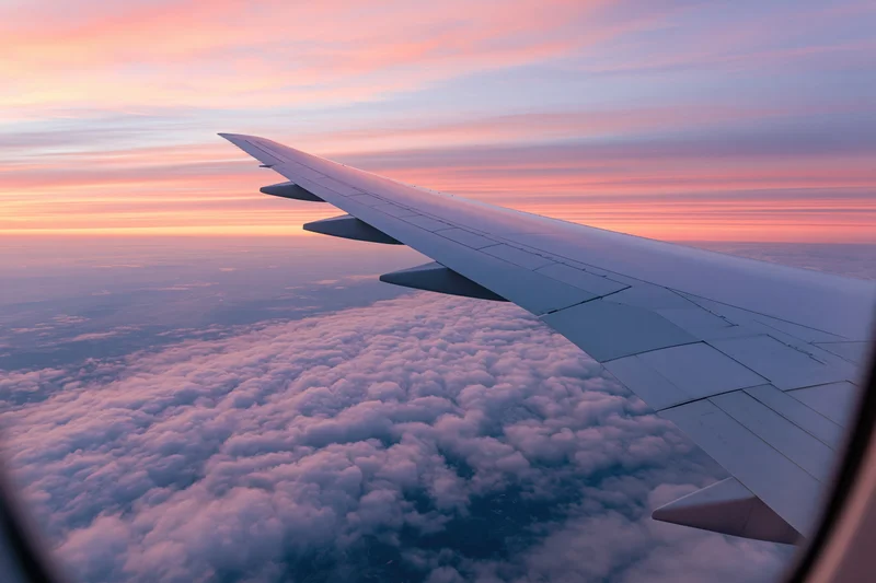 Airplane wing viewed through passenger window above cloud layer during sunset