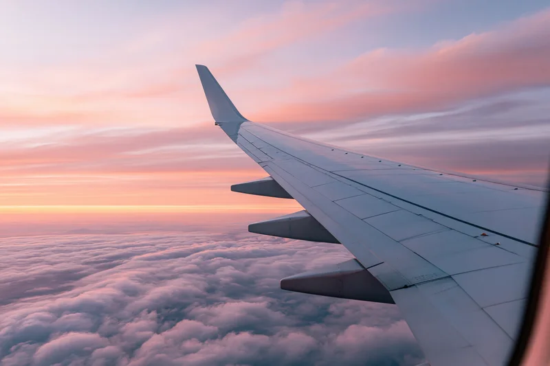 Airplane wing seen through passenger window above cloud layer during sunset