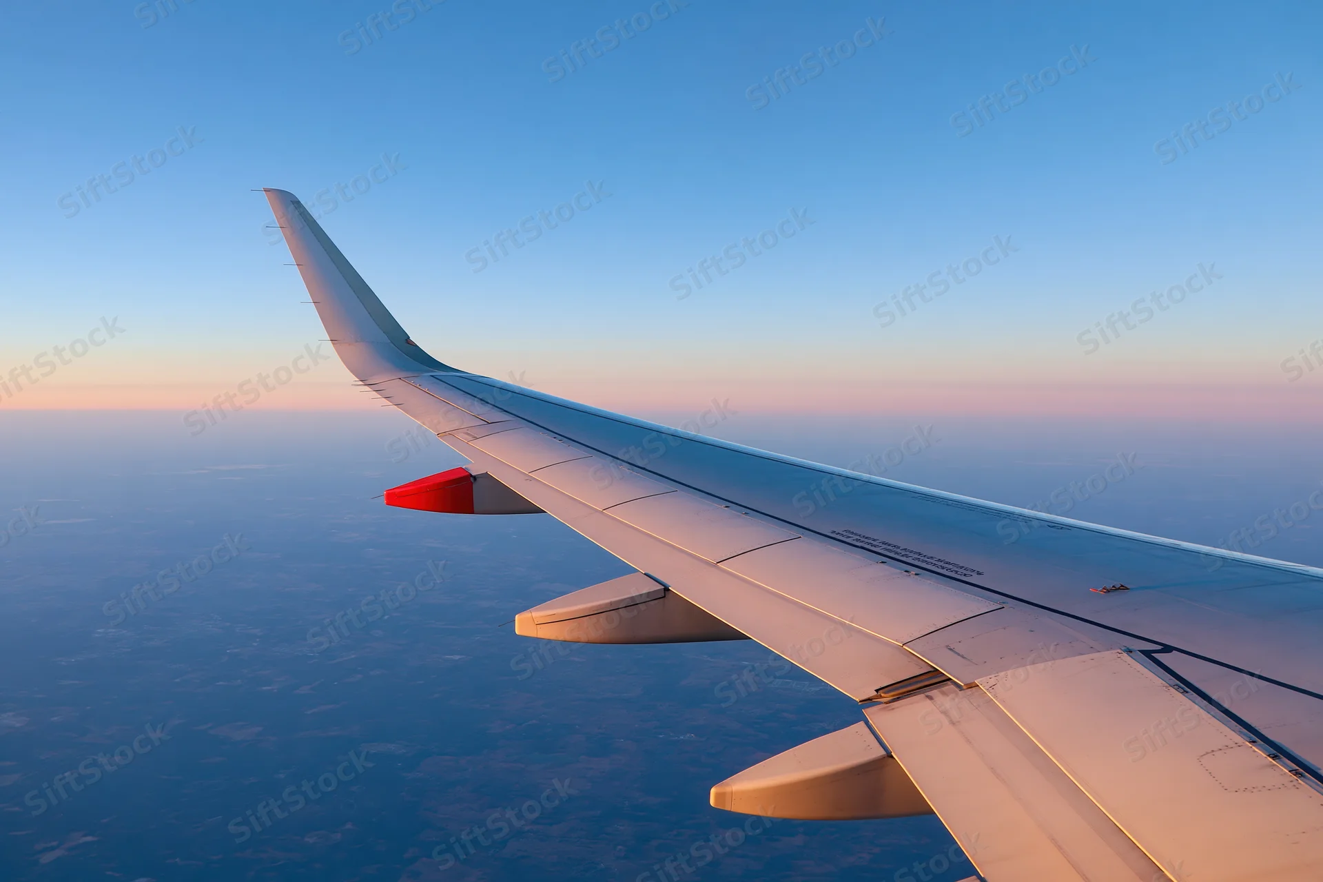 Airplane wing viewed from passenger window during cruising altitude at sunset