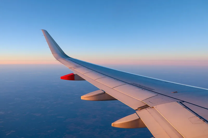Airplane wing viewed from passenger window during cruising altitude at sunset