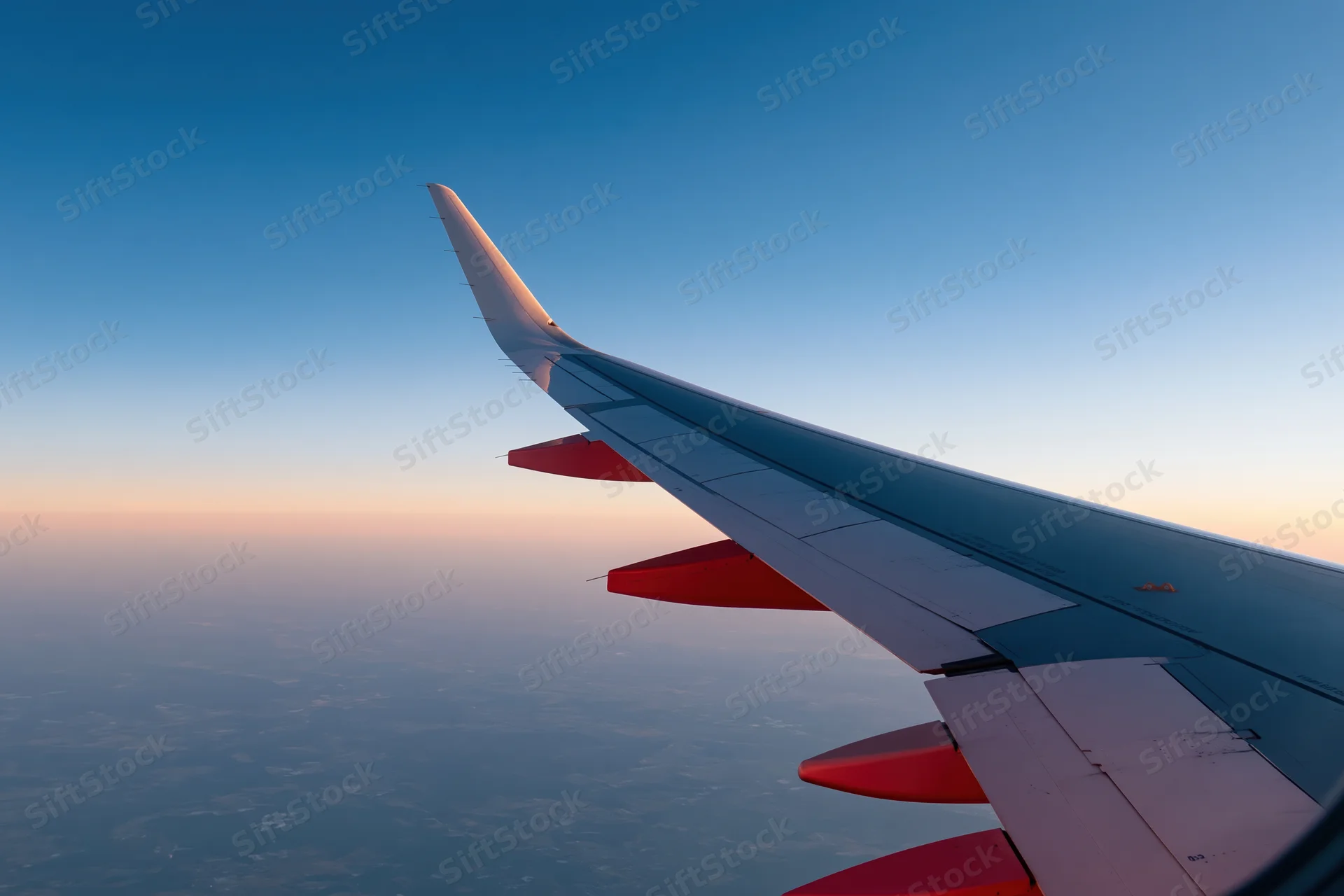 Airplane wing viewed from passenger window during cruising altitude at sunset