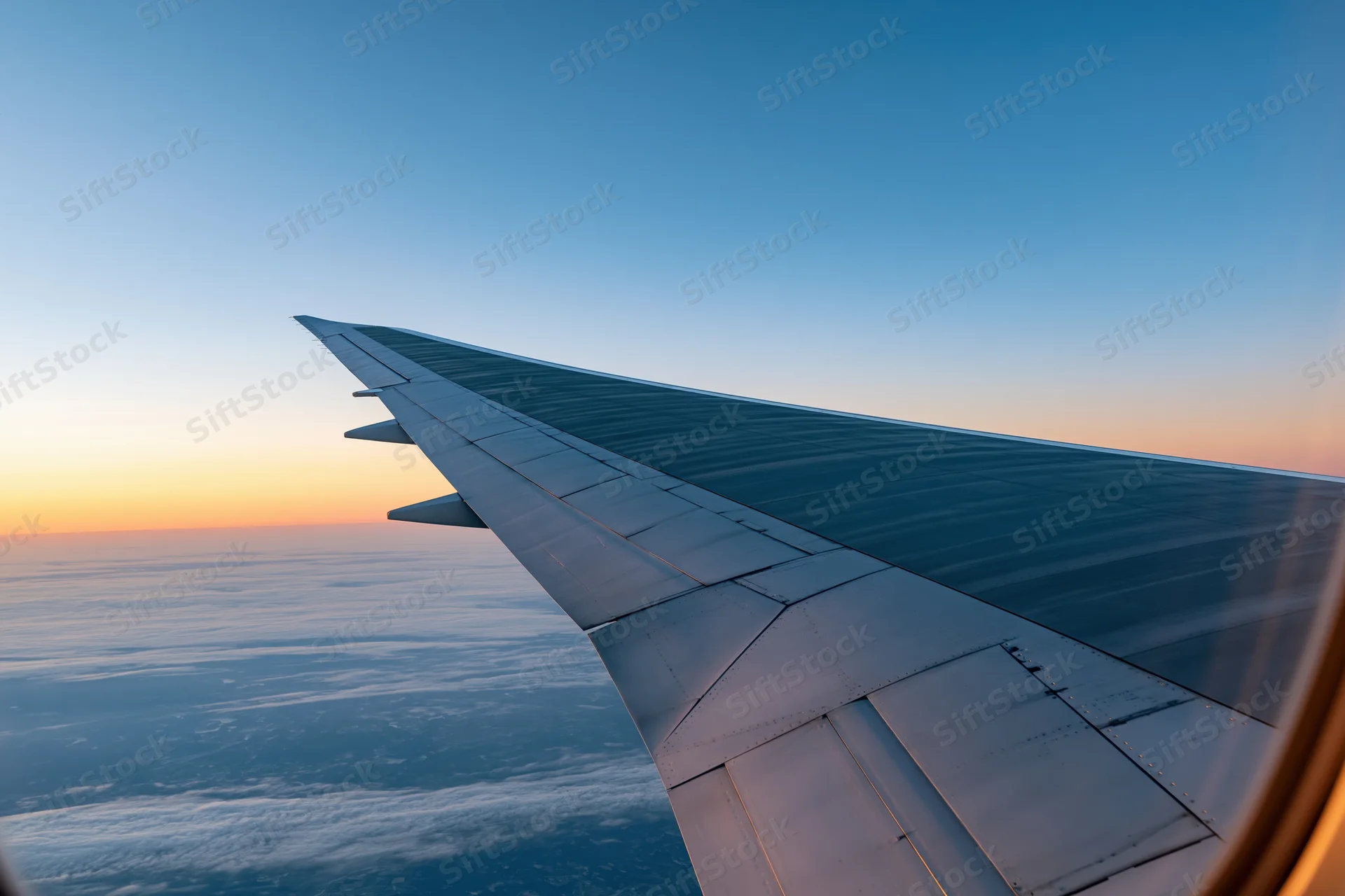 Airplane wing viewed from passenger window during cruising flight above clouds at sunset