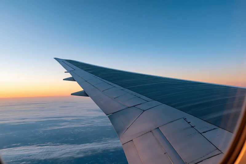 Airplane wing viewed from passenger window during cruising flight above clouds at sunset