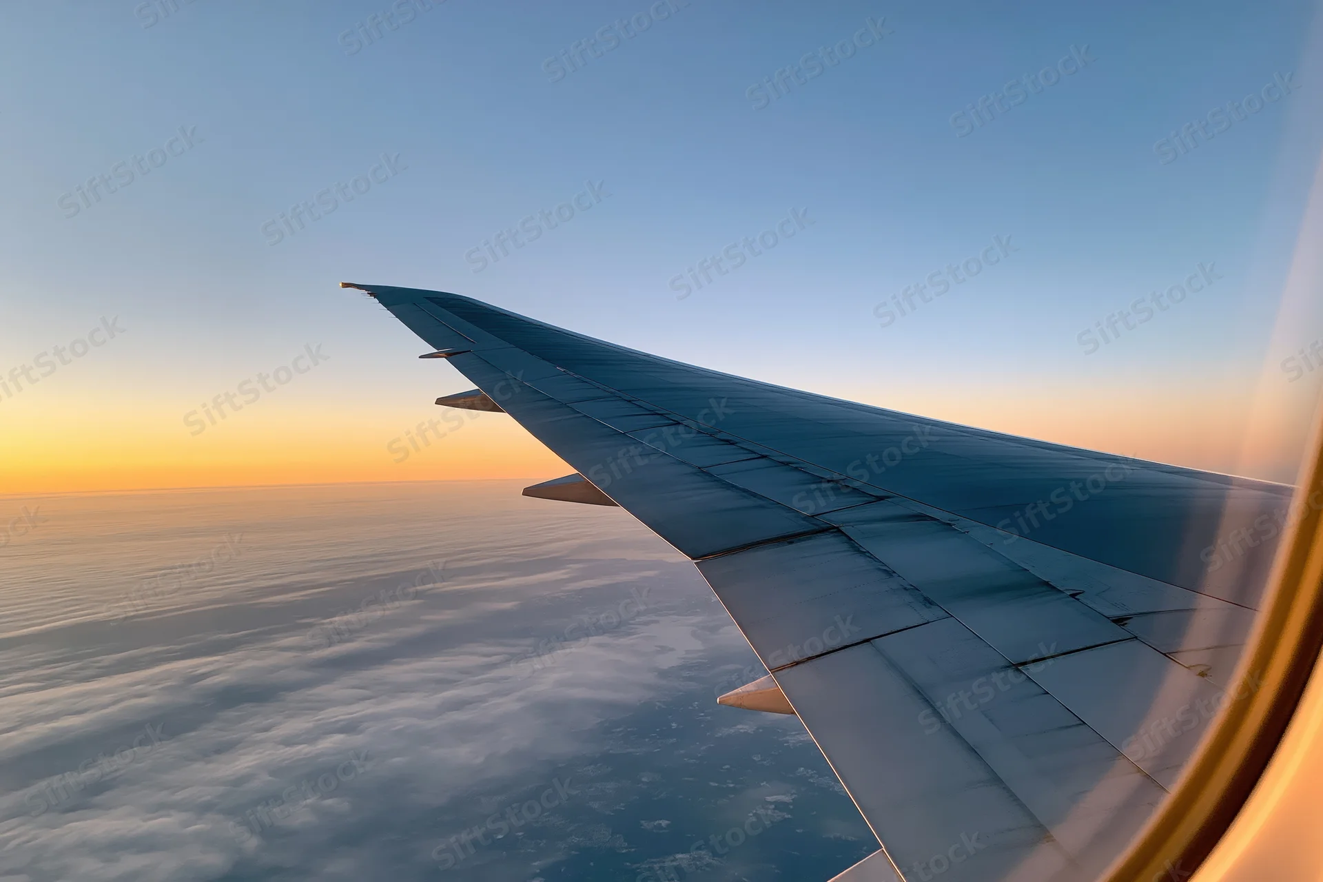 Airplane wing viewed from passenger window during cruising flight above clouds at sunset