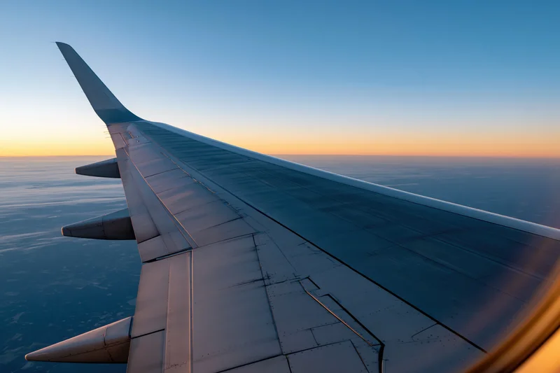 Airplane wing viewed from passenger window during cruising altitude at sunset