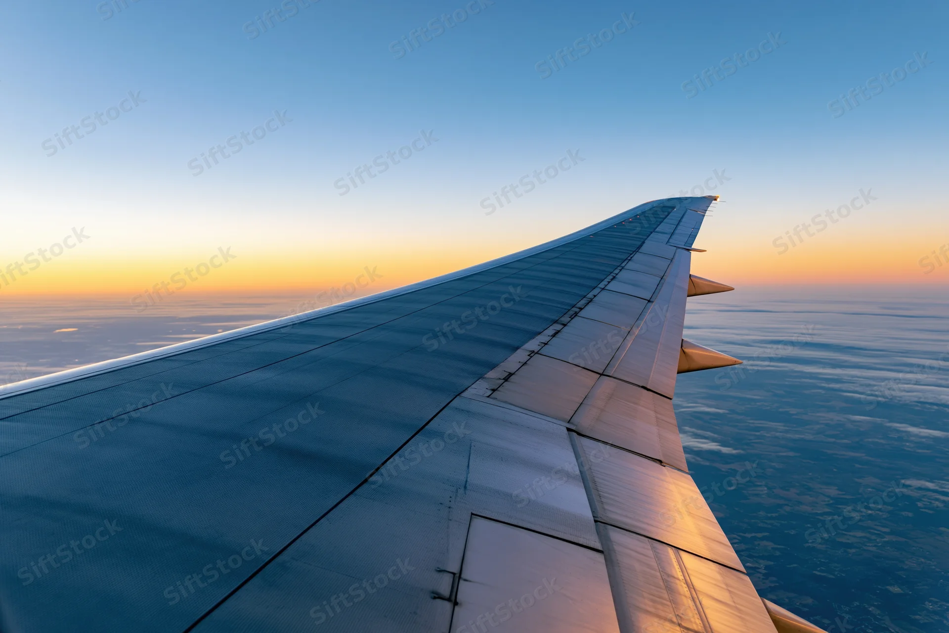Airplane wing viewed from passenger window during cruising flight above clouds at sunset