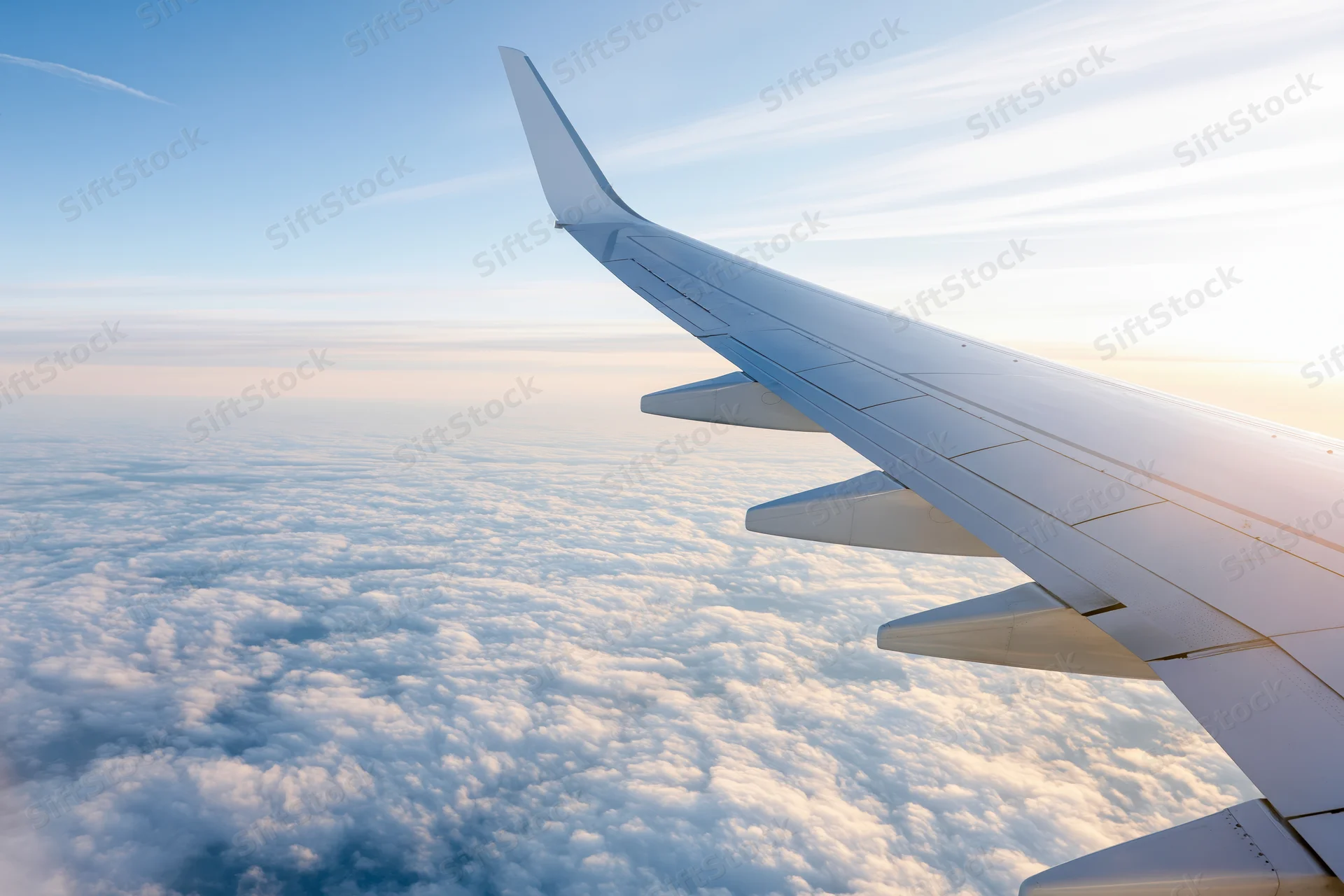 Airplane wing viewed from passenger window during cruising flight above clouds