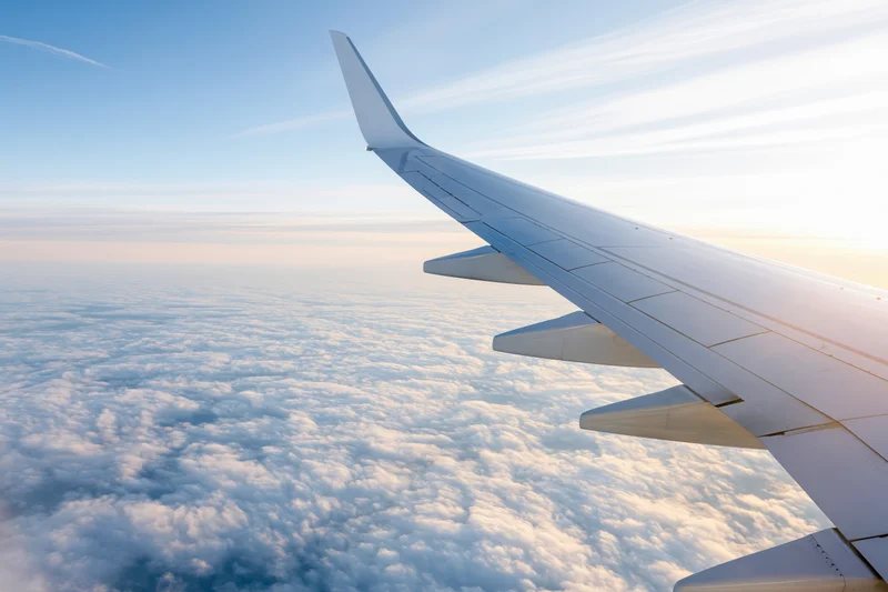 Airplane wing viewed from passenger window during cruising flight above clouds