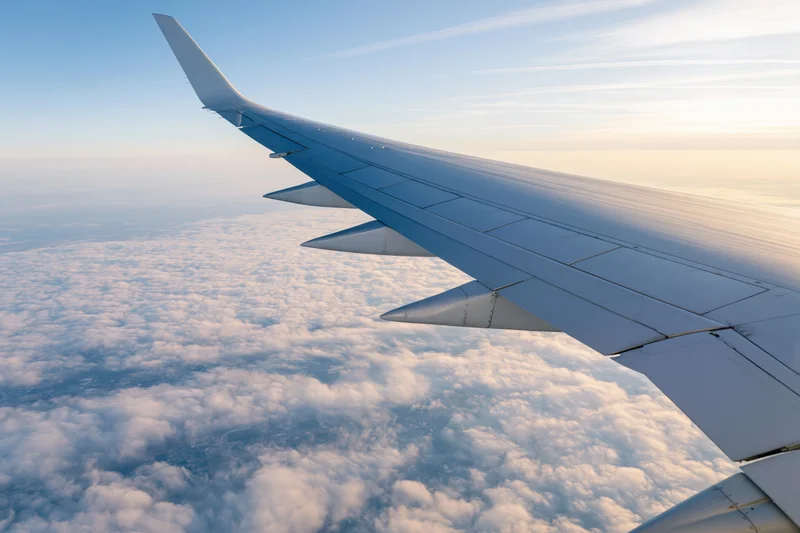 Airplane wing viewed from passenger window during cruising flight above clouds