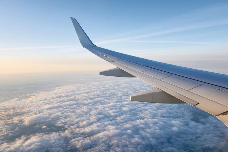 Airplane wing viewed from passenger window during cruising flight above clouds