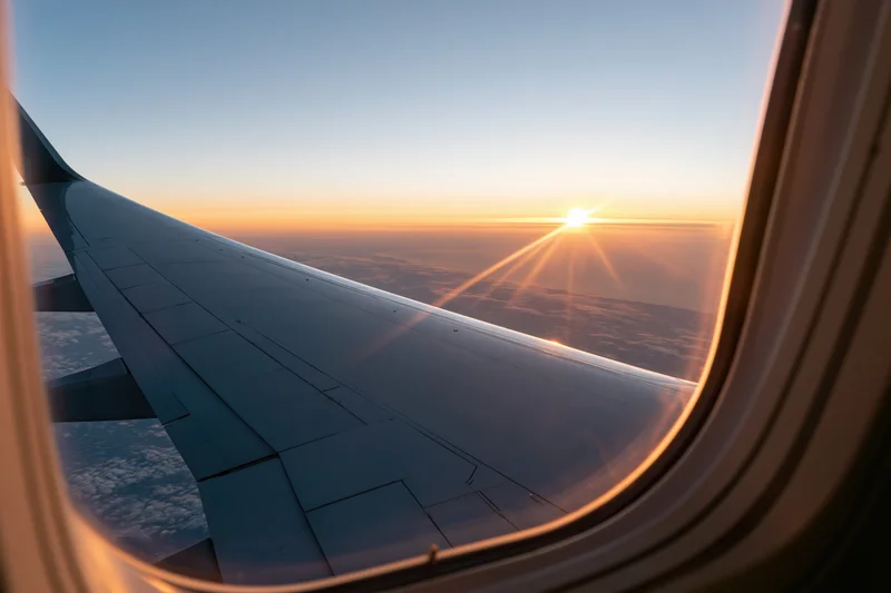 Airplane wing seen through passenger window during sunset flight above clouds