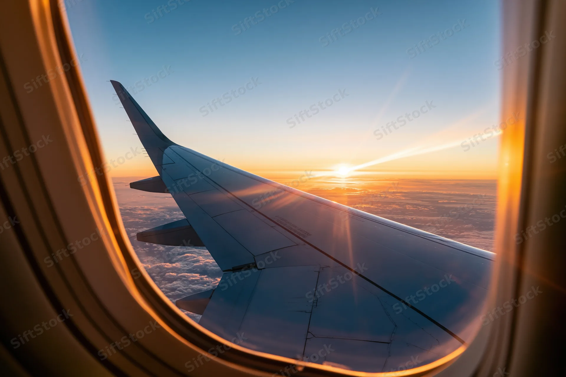 Airplane wing seen through passenger window during sunset flight above clouds