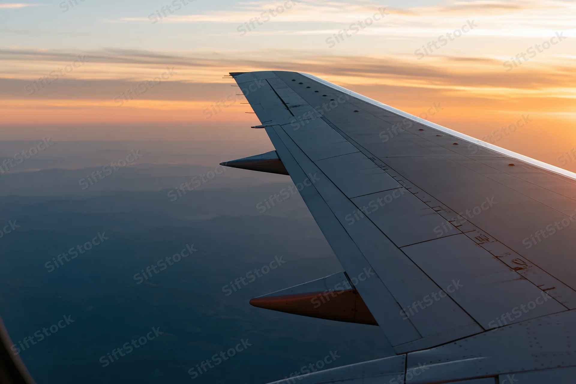 Airplane wing viewed through passenger window during sunset cruise at high altitude