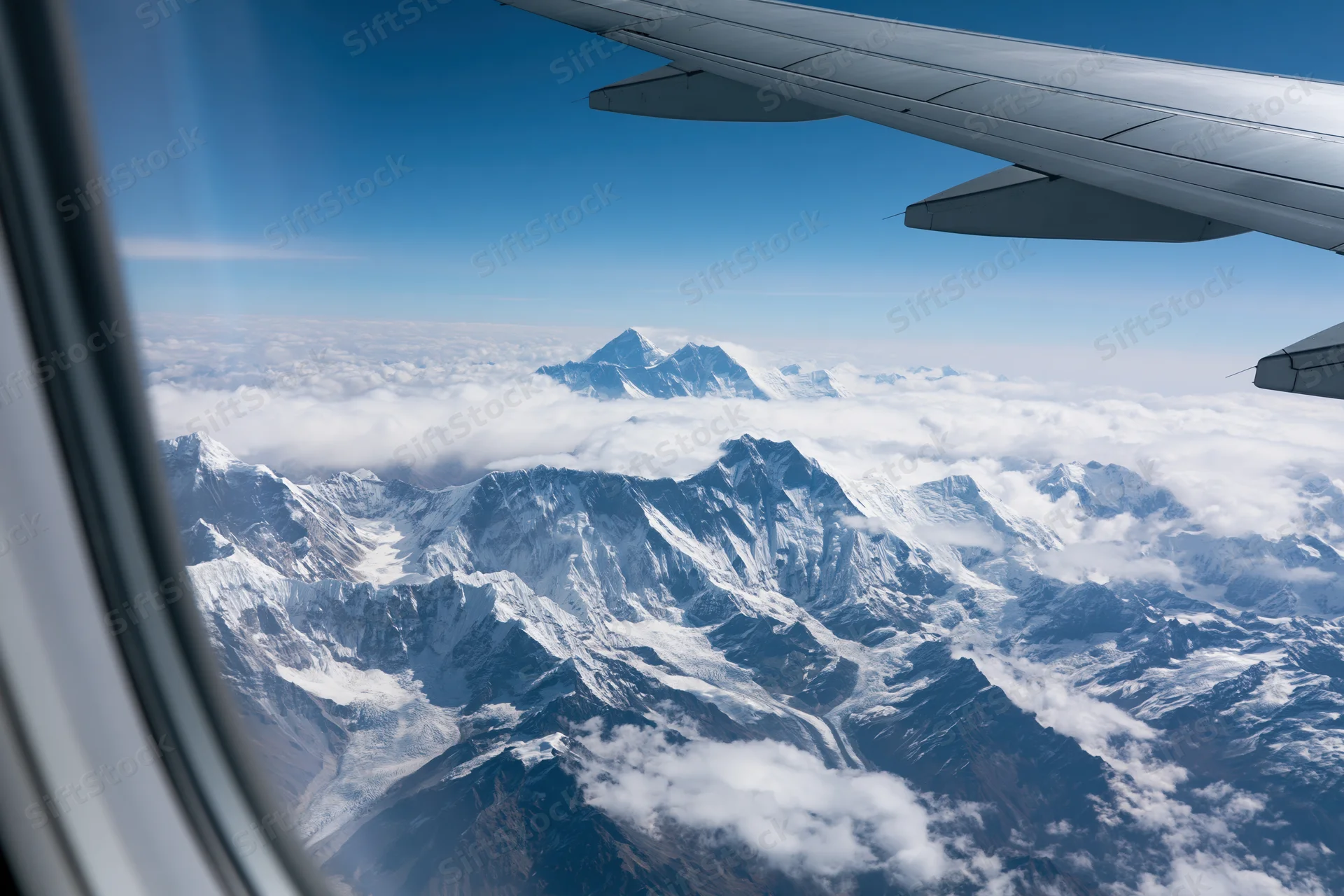 Airplane wing viewed from window above snow-covered mountains and clouds