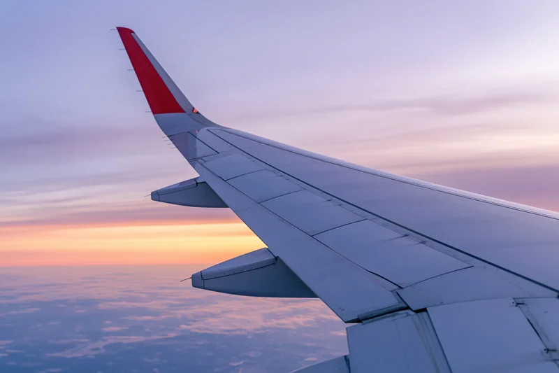 Airplane wing with red tip viewed from passenger window during sunset above clouds
