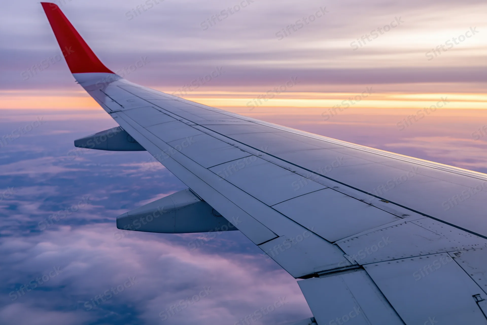 Airplane wing with red tip viewed from passenger window above clouds at sunset