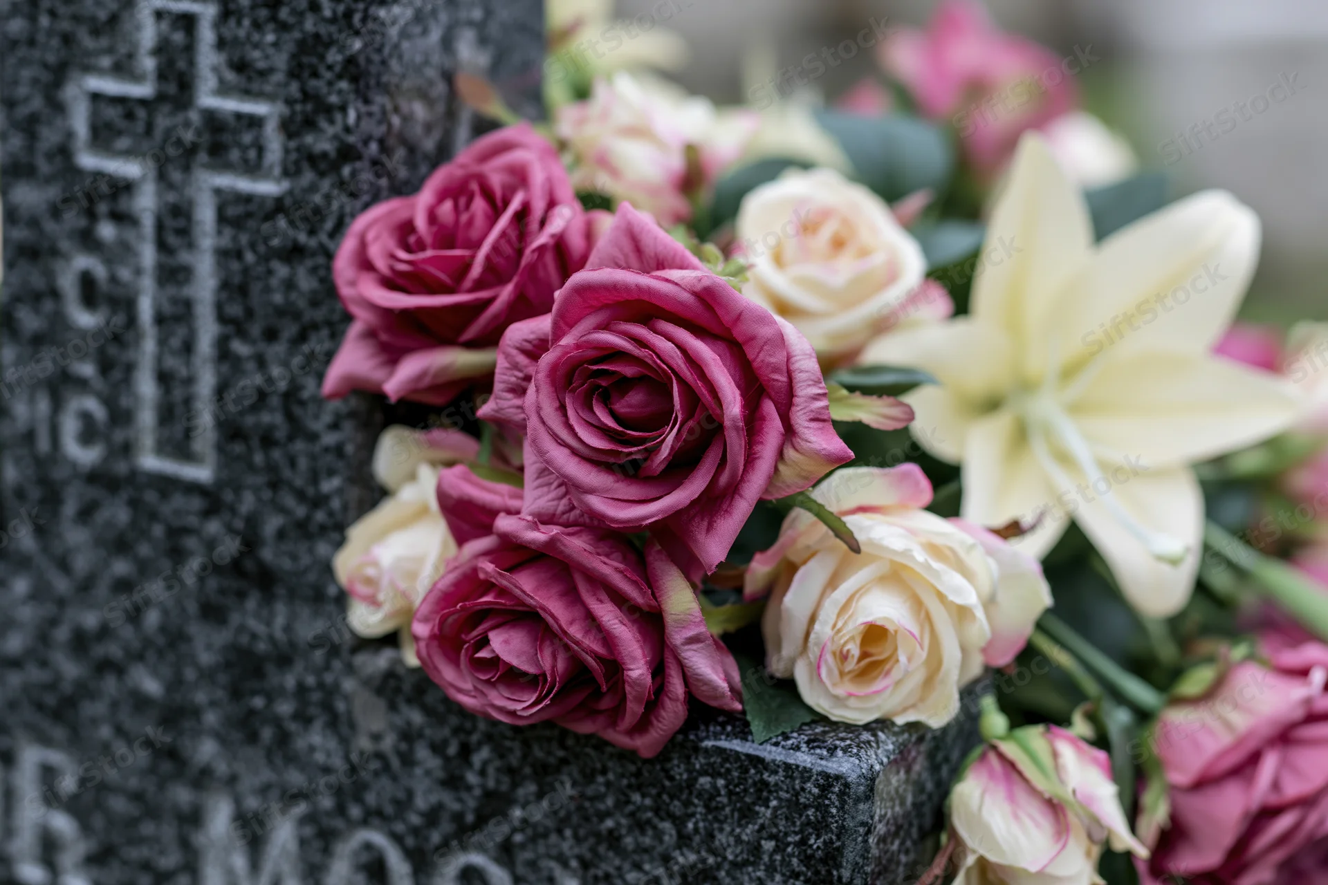 Artificial flower arrangement with pink and white roses and lily on a grave stone