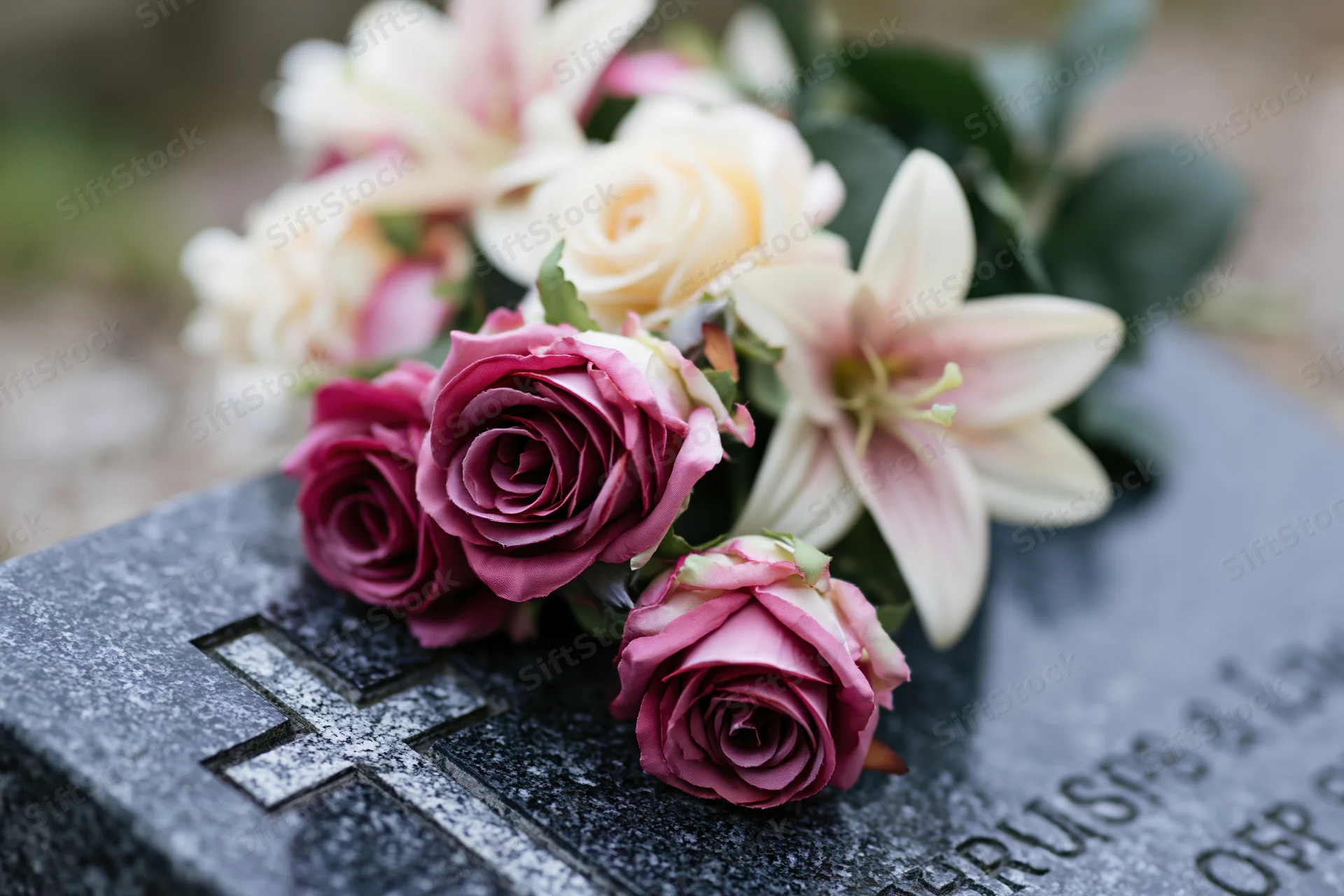 Artificial flower arrangement with pink roses and white lilies on a grave marker