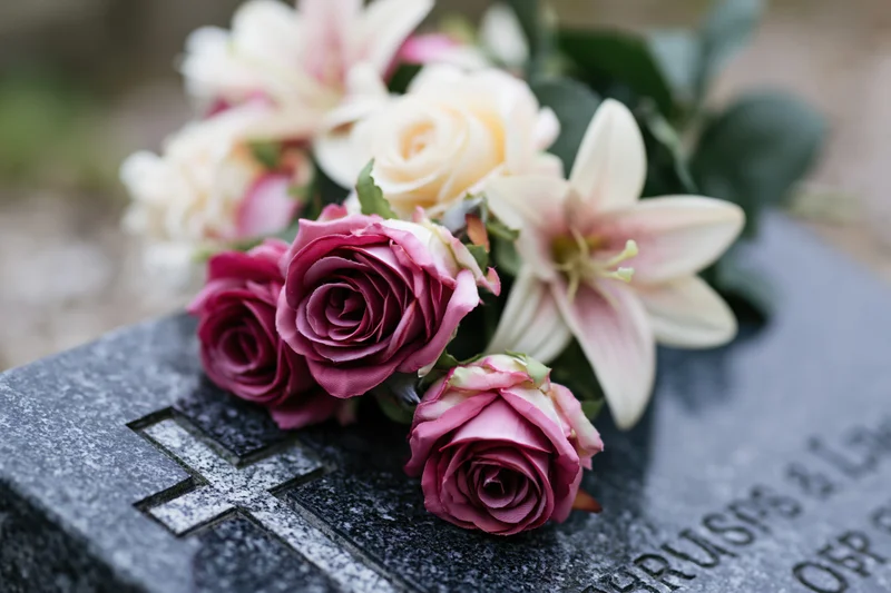 Artificial flower arrangement with pink roses and white lilies on a grave marker