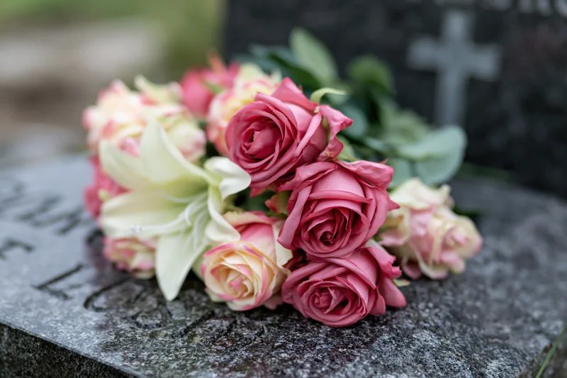Artificial flower arrangement with pink roses and white lilies on a grave stone