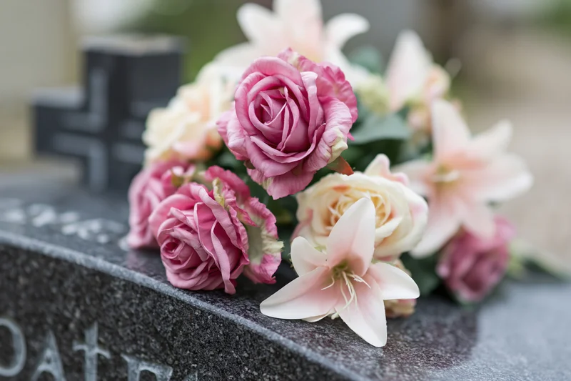 Artificial pink and cream roses arranged on a granite tombstone in a cemetery