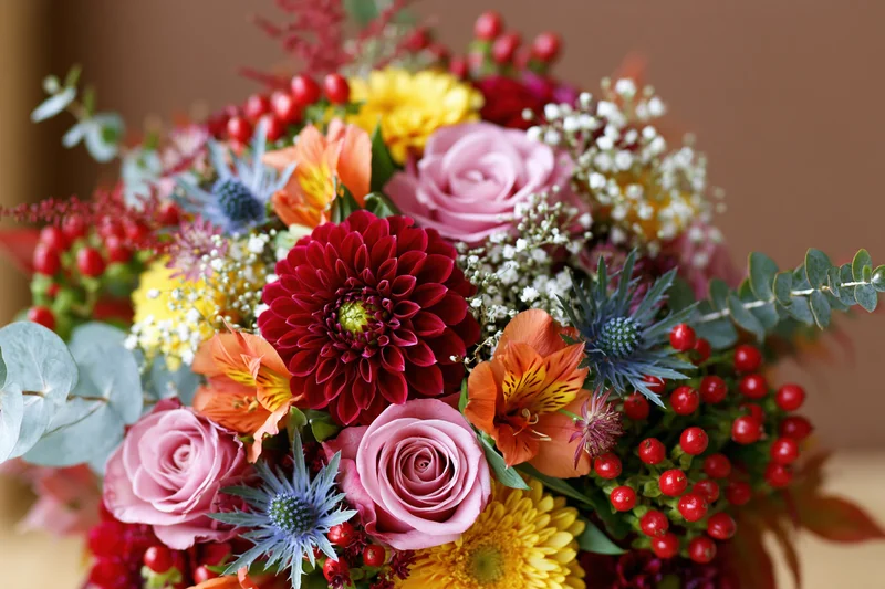 Densely packed autumn floral bouquet with pink roses, red dahlias, orange alstroemeria, and green eucalyptus foliage