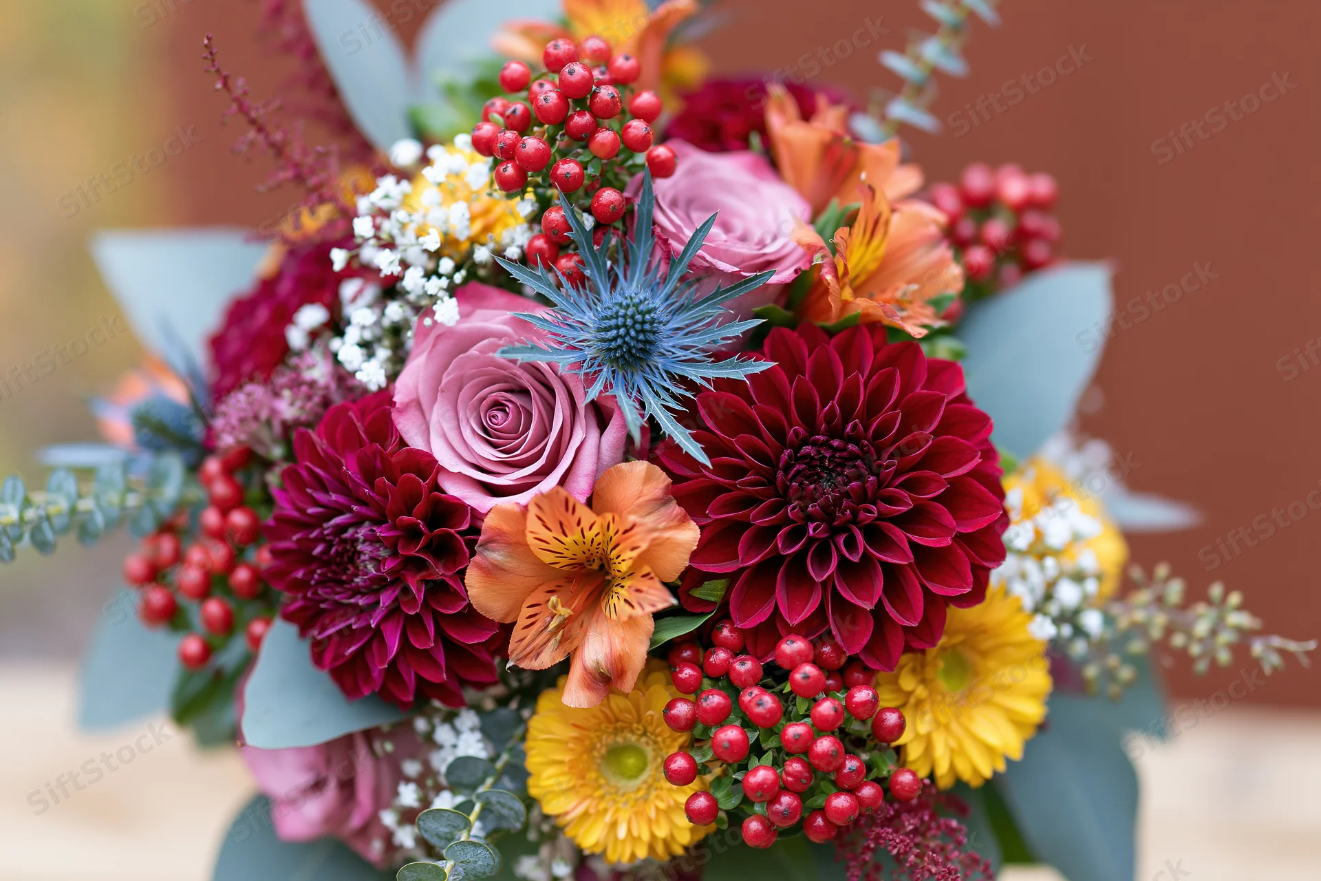 Autumn floral bouquet densely packed with pink roses, deep red dahlias, orange alstroemeria, red berries, and green foliage