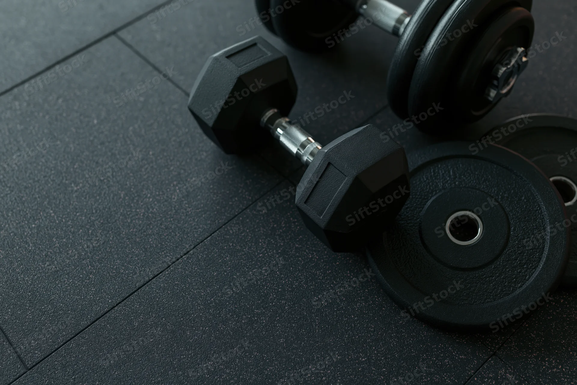 Black hexagonal dumbbell and weight plates resting on dark rubber gym floor